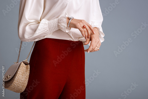 Close up of fashionable elegant woman`s outfit: trendy small  shoulder bag, stylish wrist watch, beautiful ring with red gem. Model posing on blue background. Copy, empty space for text
