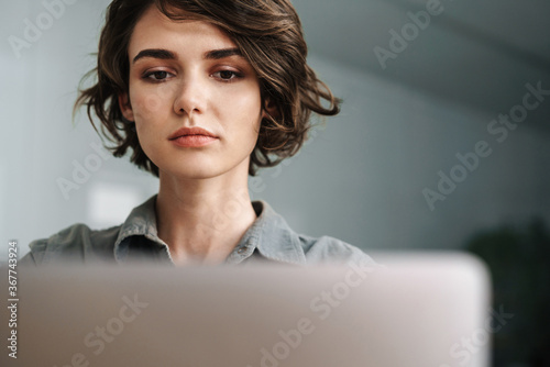 Foto Image of young focused woman working with laptop while sitting at table