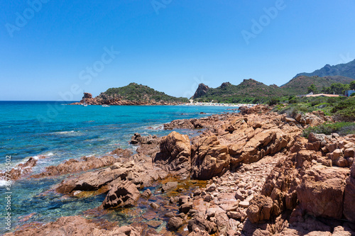 landscape, red rock above a blue bay in the beach of Su Sirboni