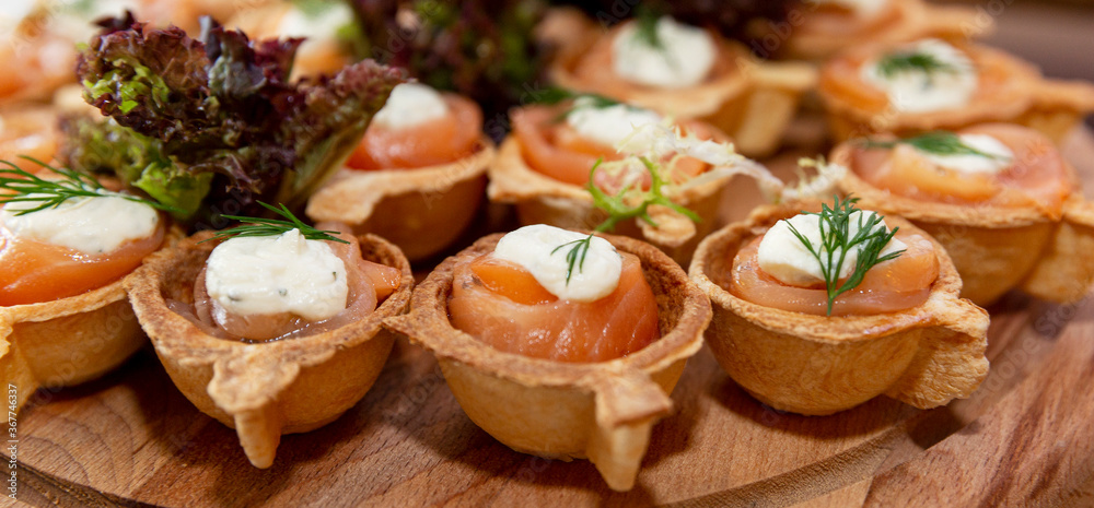 Appetizing snacks at the buffet table. Tartlets with fish and soft cheese. Close-up. Panorama format.