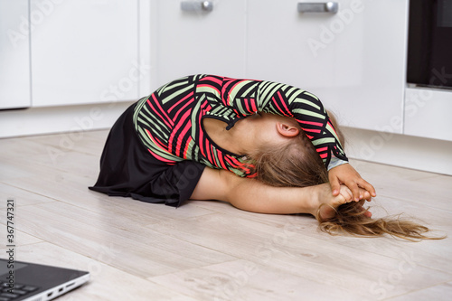 little girl doing gymnastics at home in the kitchen on a warm floor photo