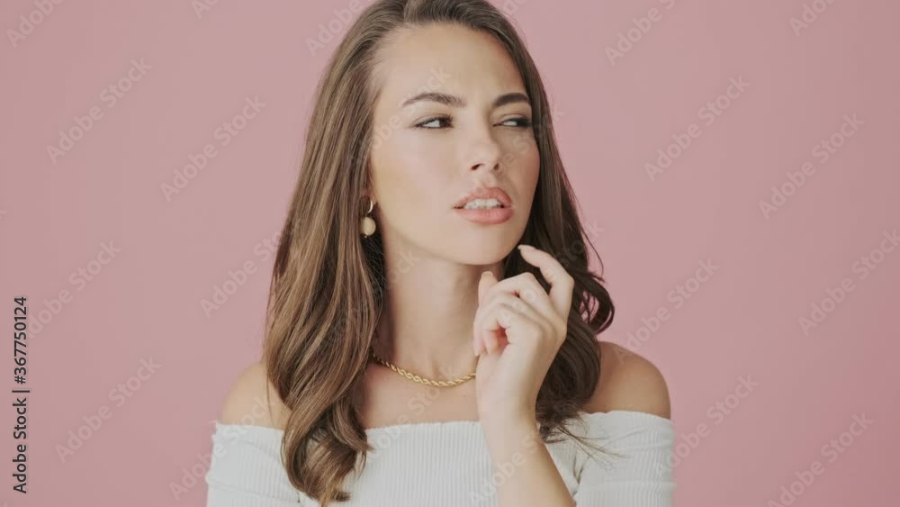 A serious young woman is thinking about something standing isolated over pink background in studio A serious young woman is thinking about something standing isolated over pink background in studio