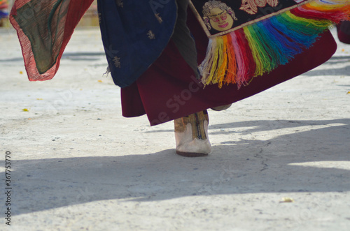 Details of a white shoe and colourful fabrics of a dancing monk in a temple in India.