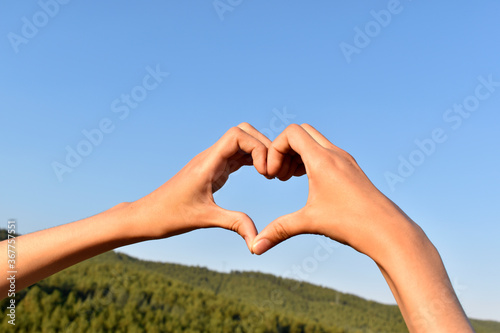 hands folded in the shape of a heart against the background of mountains and sky
