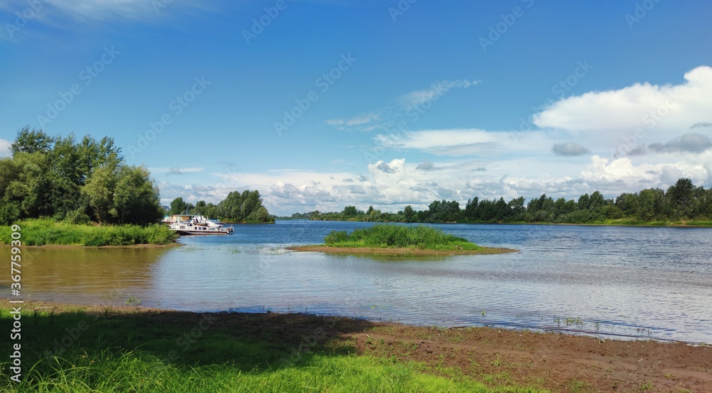 Obraz premium sunny landscape with blue sky over green river bank with moored boats