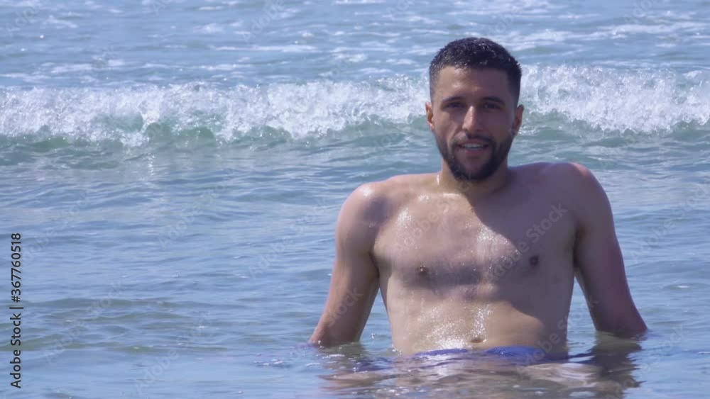 Young handsome man is sitting in the waves of the sea surf and enjoys a sea vacation Young handsome man is sitting in the waves of the sea surf and enjoys a sea vacation