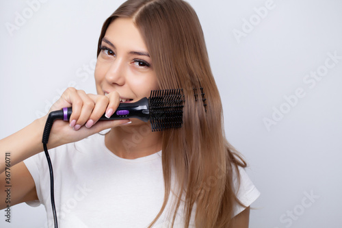 Pretty girl with beautiful hair straightens her hair with a hot curling iron
