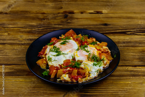 Homemade breakfast shakshuka - fried eggs, onion, bell pepper, tomatoes and dill on rustic wooden table. Jewish cuisine