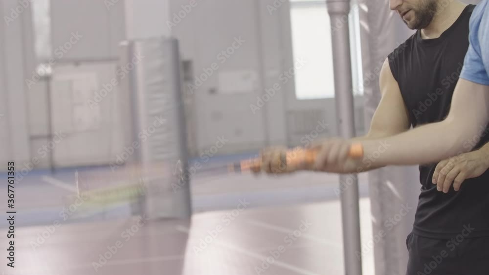 Side view of unrecognizable sportsmen practicing hand movement in badminton. Two Caucasian men moving hands holding rackets. Sport game training indoors.