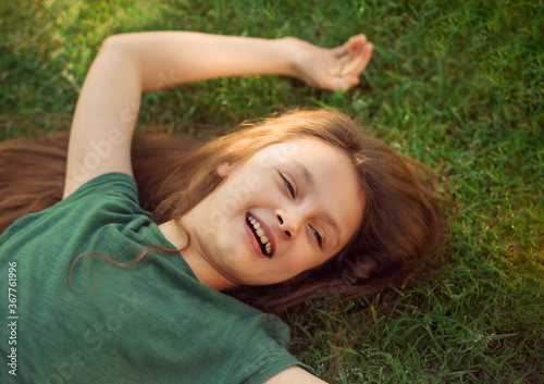 Happy laughing relaxing kid girl lying on the grass on nature summer background. Closeup positive outdoors bright sunny