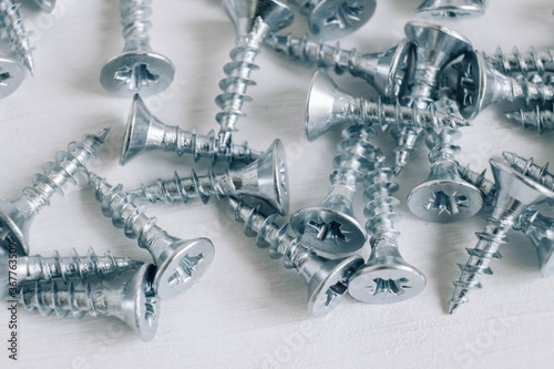 Metal tapping screws for wood on white wooden background. Construction equipment concept. Top view. Copy, empty space for text
