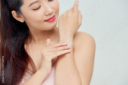 Smiling young woman applies cream on her hands. On a white background.