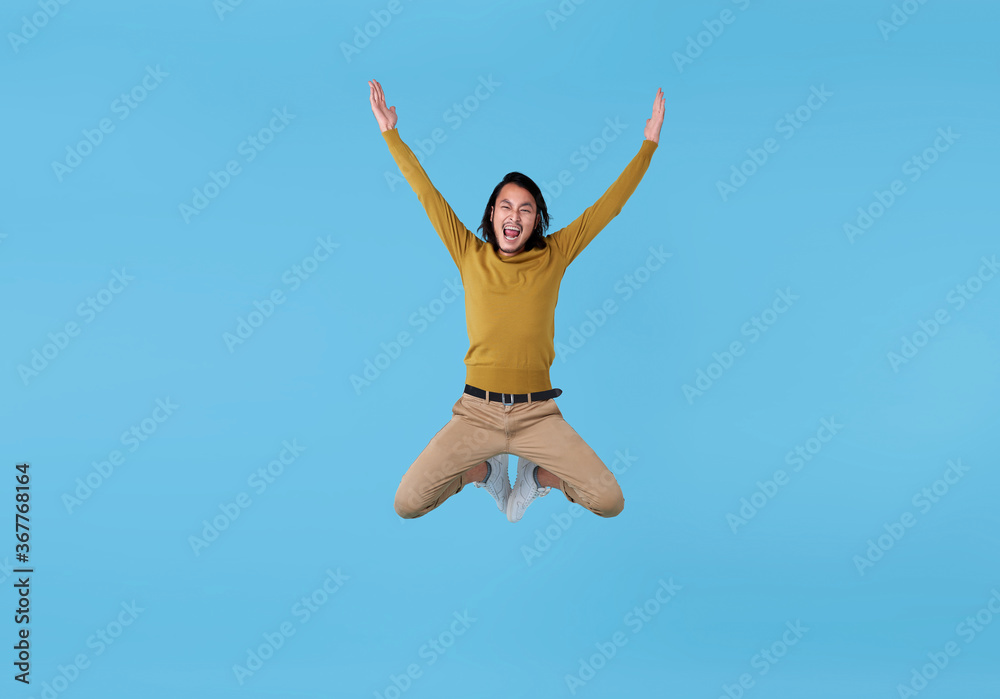 Happy energetic young Asian man jumping in mid-air isolated on blue background. Happy energetic young Asian man jumping in mid-air isolated on blue background.