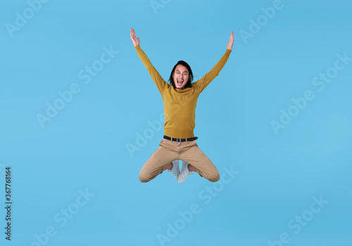 Happy energetic young Asian man jumping in mid-air isolated on blue background.