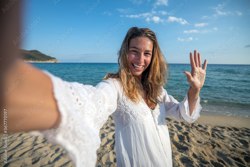 A happy carefree young female tourist is making selfie or technology video call to a friends or parents on a desert offshore seaside in a sunny day during vacation trip. A happy carefree young female tourist is making selfie or technology video call to a friends or parents on a desert offshore seaside in a sunny day during vacation trip.