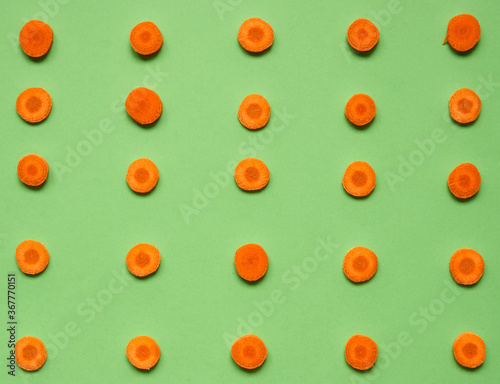 Flat lay composition with sliced carrot on green color background. Pattern. Top view, close up. Selective focus..