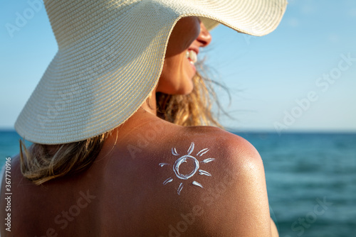 An young woman with applied sun shape of sunscreen or sun tanning lotion on a shoulder to take care of her skin on a seaside beach during holidays vacation.