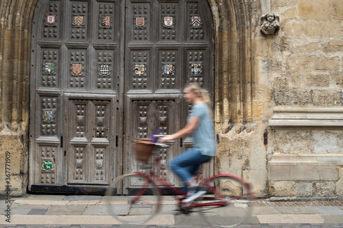 Female Student Riding Old Fashioned Bicycle Around Oxford University College Buildings With Motion Blur