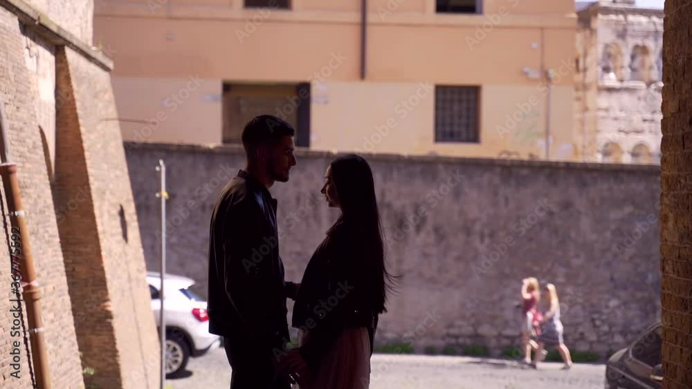 silhouette of a stylish young couple of hipsters in the arch of a building on the street holding hands and hugging. Girl and guy meet on urban background. Tourists in love feel good. Slow motion silhouette of a stylish young couple of hipsters in the arch of a building on the street holding hands and hugging. Girl and guy meet on urban background. Tourists in love feel good. Slow motion