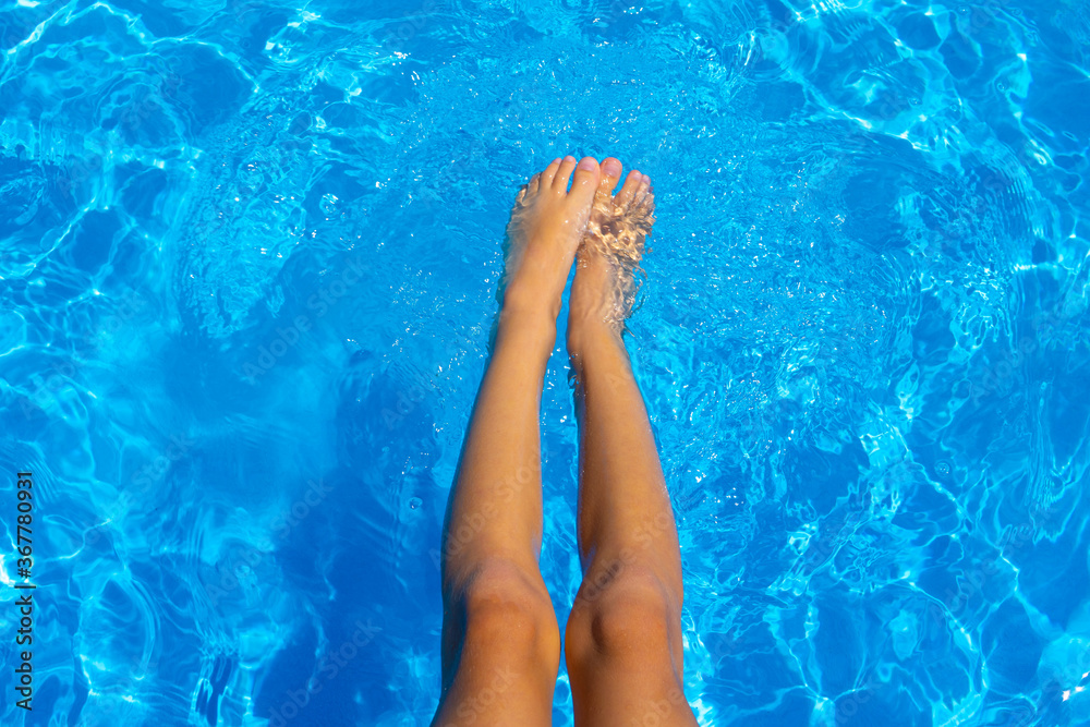Child feet in the pool. Soft focus background. Summer vacation. Beautiful closeup for luxury lifestyle design.Vacation, holiday. Beautiful closeup of child feet pool on blue background.