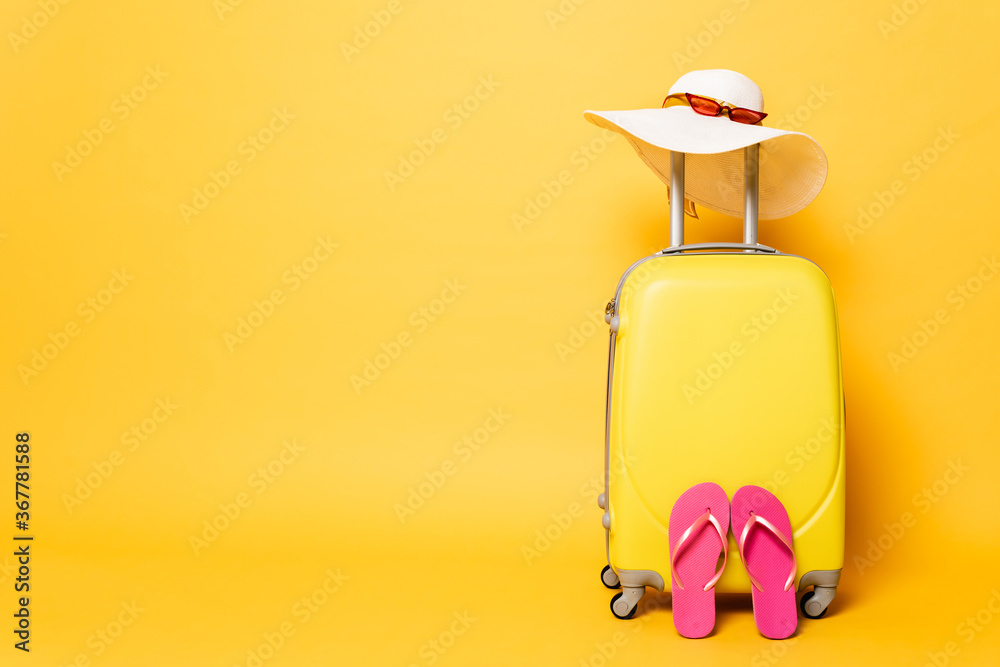 yellow travel bag with flip flops, sun hat and sunglasses isolated on yellow - obrazy, fototapety, plakaty 