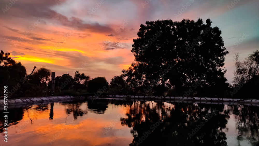 Orange clouds at evening time, clouds reflection in pond water