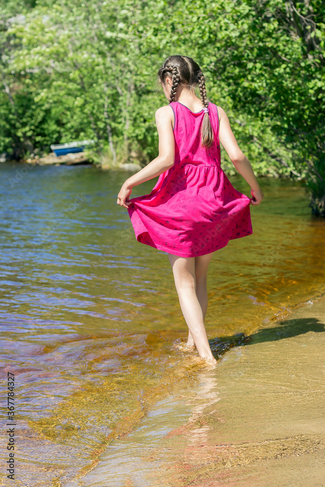 A girl walks along the coastline with bare feet on clean warm water on a summer day. A girl walks along the coastline with bare feet on clean warm water on a summer day.