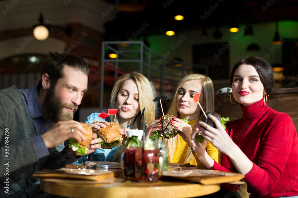 People have dinner together at a table in a cafe. Happy friends eat burgers and drink cocktails in the restaurant