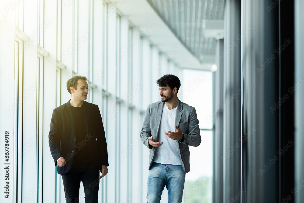 Confident business partners walking down in office and discussing work Confident business partners walking down in office and discussing work