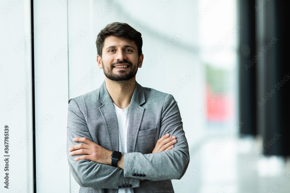 Confident businessman standing with arms folded at modern office