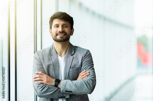 Confident businessman standing with arms folded at modern office