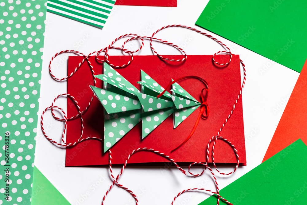 Fototapeta premium Handmade New Year postcard with paper christmas fir tree. Holiday idea for family time and gift for beloved. Fine motor skills, creativity development and fun. Traditional colors: green, red.