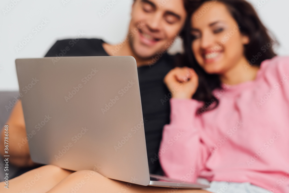 Selective focus of positive couple using laptop on sofa isolated on grey