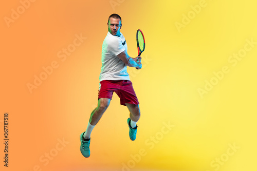 In jump. One caucasian man playing tennis on studio background in neon light. Fit young professional male player in motion or action during sport game. Concept of movement, sport, healthy lifestyle. © master1305