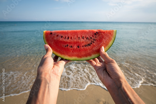 POV shot of a woman hands is showing a fresh juicy watermelon in camera on a seascape background during summer holidays vacation trip at sea.