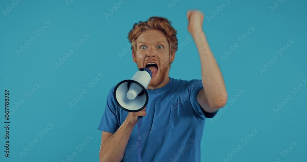bearded redhead man yelling in megaphone isolated on blue