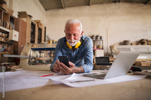 Foto Likeable older carpenter is looking at the cellphone and smiling