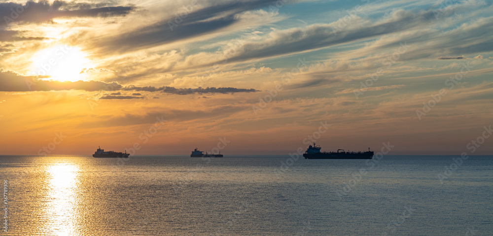 Silhouette of ships on background out at sea at cloudy sunset