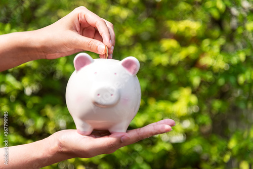 Close up hands holding piggy and putting a coin into piggy bank for future life. Investment and Saving Concept.