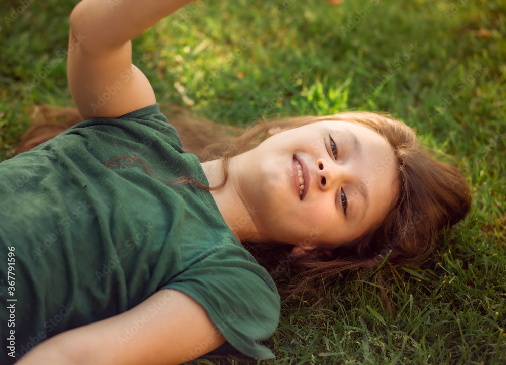 Happy laughing fun kid girl lying on the grass on nature summer background. Closeup positive outdoors bright sunny Happy laughing fun kid girl lying on the grass on nature summer background. Closeup positive outdoors bright sunny