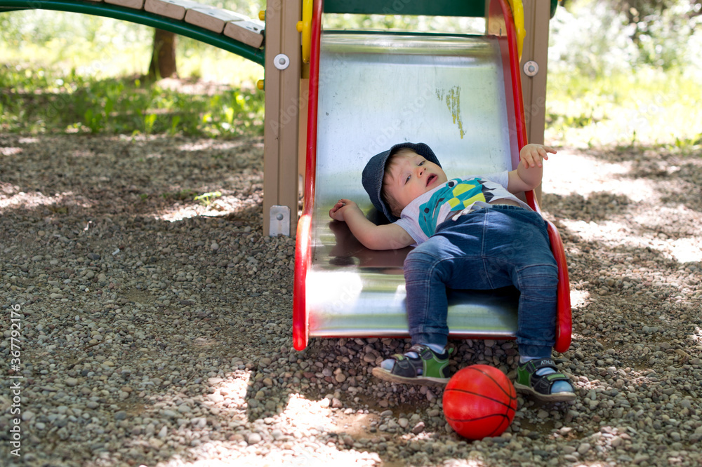 Obraz premium 2-year old boy in a playground. summer day in the yard. child sliding down a slide. happiness of carefree childhood.