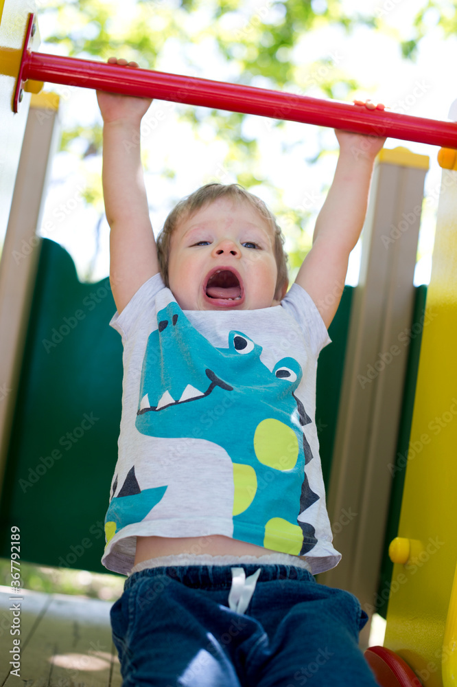 2-year old boy in a playground. summer day in the yard. child sliding down a slide. happiness of carefree childhood.