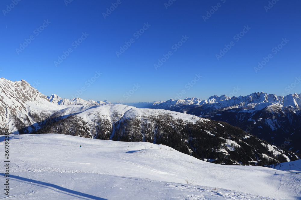Obertilliach ski resort in west Austria in Tyrol. Panorama on Gailtal Alps with blue sky from top of Golzentipp. Scenery of ski slopes and snow mountains peaks