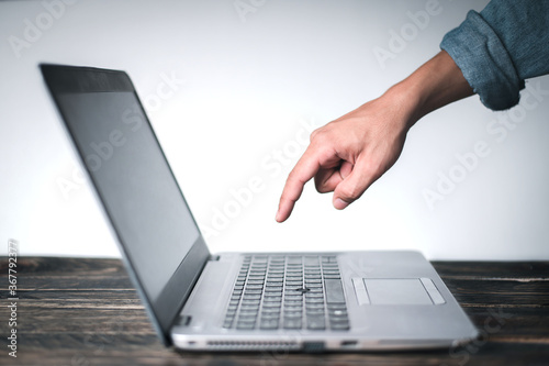 A man's hand wearing a denim shirt showing a gesture pointing at the computer on the table, On a white background, Business concept, Technology concept.