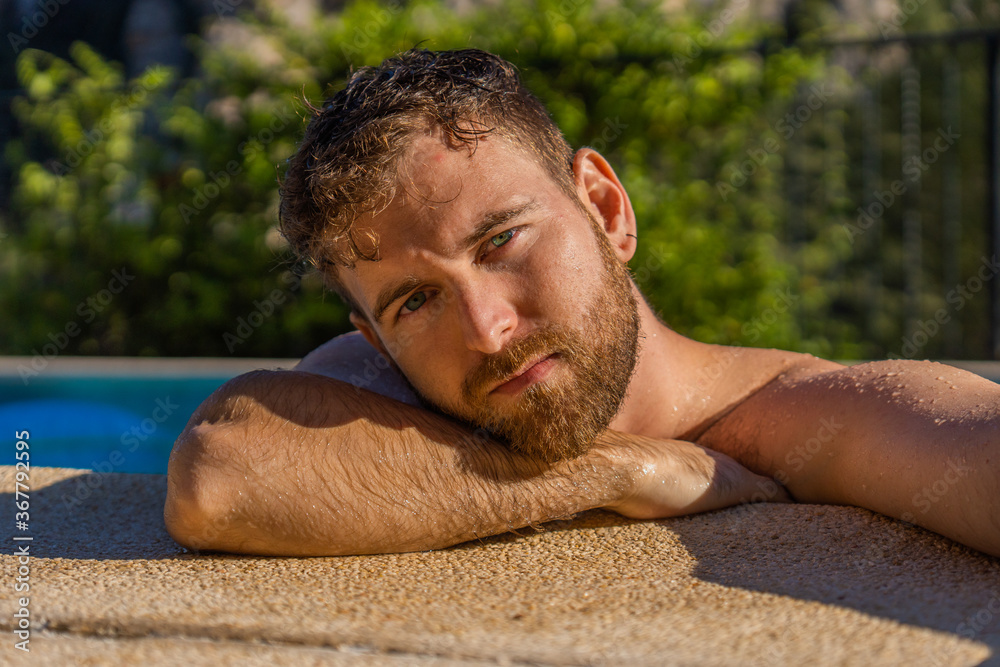 portrait of blond boy with blond short beard and green and blue eyes with northern features in a pool with mountains in the background and warm sunlight on his face portrait of blond boy with blond short beard and green and blue eyes with northern features in a pool with mountains in the background and warm sunlight on his face