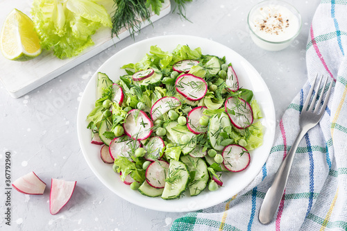 Fresh salad of cucumbers, radishes, green peas and herbs in white bowl.