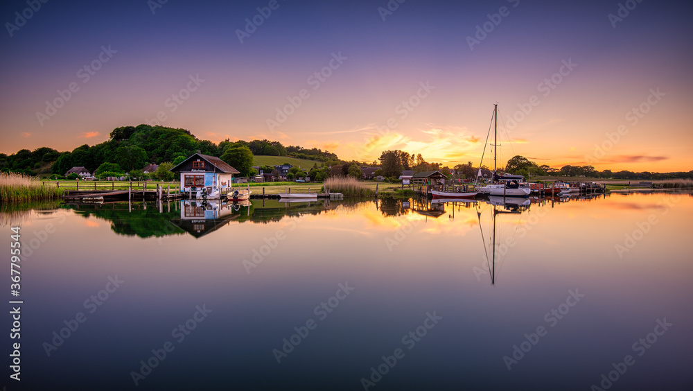 Panoramic shot of a sunset with a cabin and a boat with their reflections on the sea.