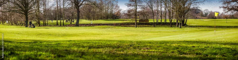 Panorama vom Golfplatz mit Fairway und Putting Green mit gelber Fahne und Golfspieler in der Ferne