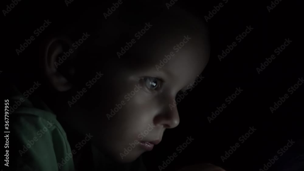 Little boy watching cartoon or playing games on smartphone at night. using your smartphone or tablet. Night shot.