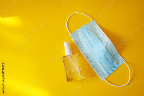 Hand sanitizer and medical protective mask on yellow background. New normal after quarantine. Copy space.